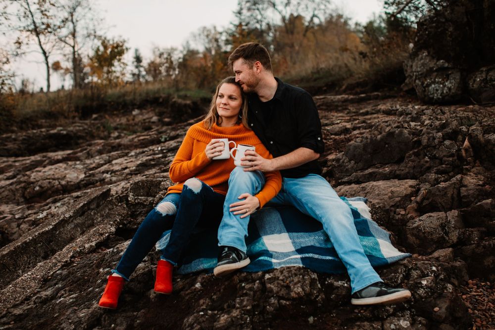 Couple shares cozy moment on blanket over rocky terrain during autumn sunset.