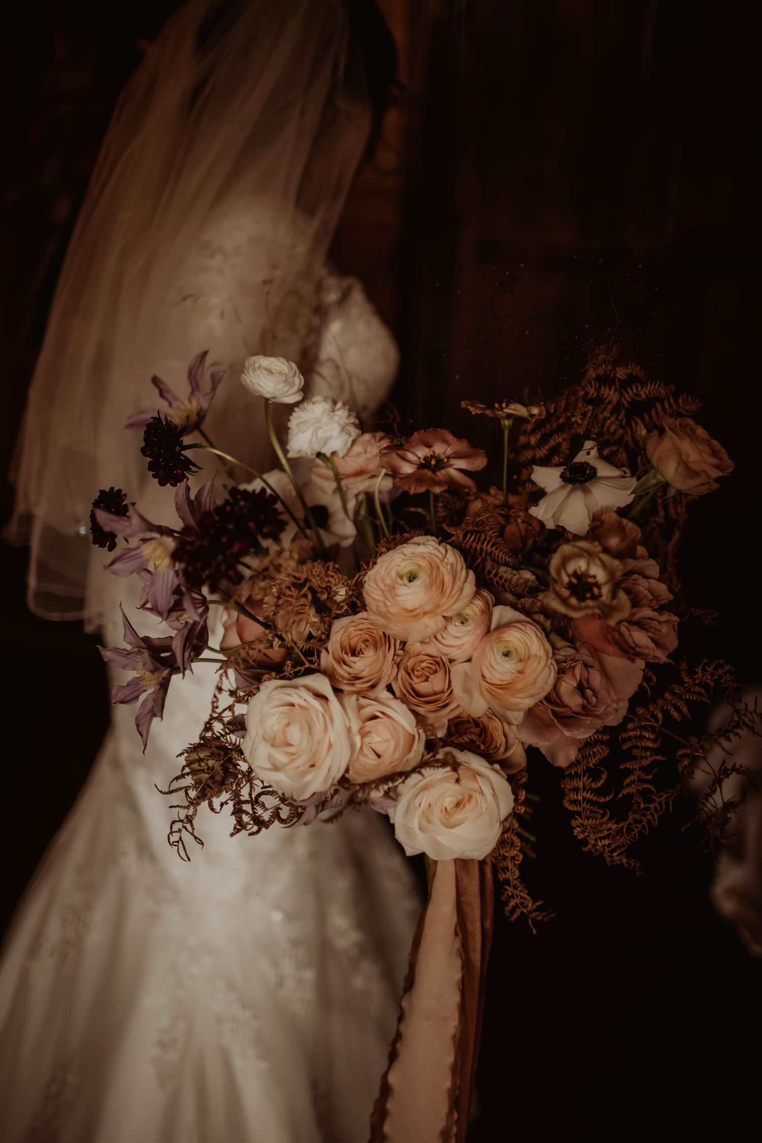 A dreamy close-up of a bridal bouquet with peach roses and dark foliage.