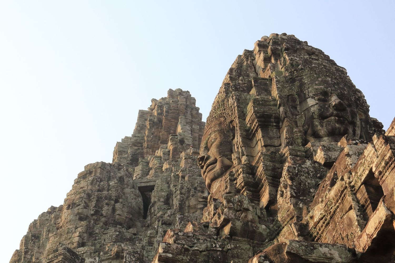 Ancient stone temple spires rise against blue sky at Angkor archaeological complex.