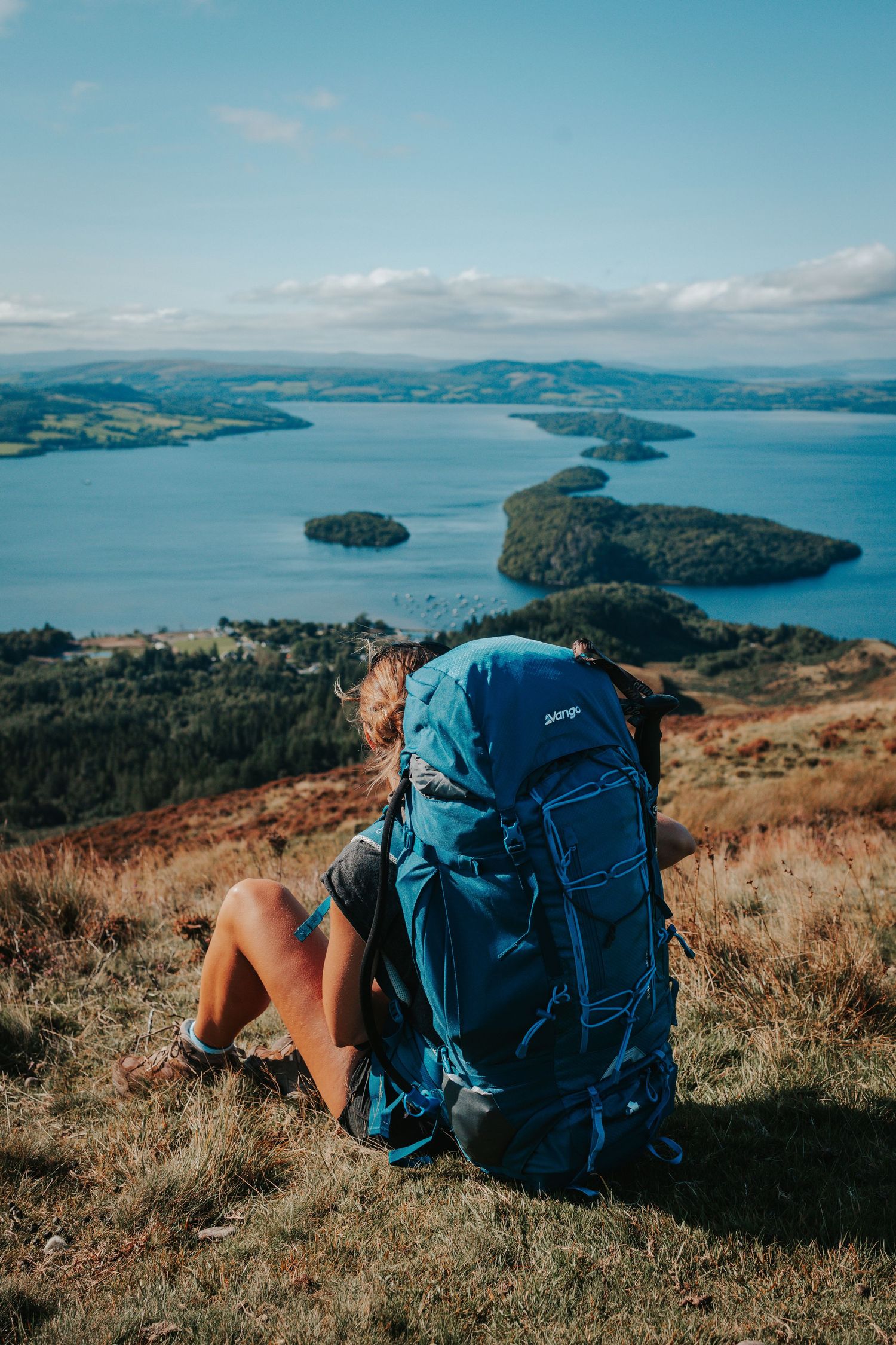 Blue backpack overlooking scenic lake vista with islands and mountains in the distance.