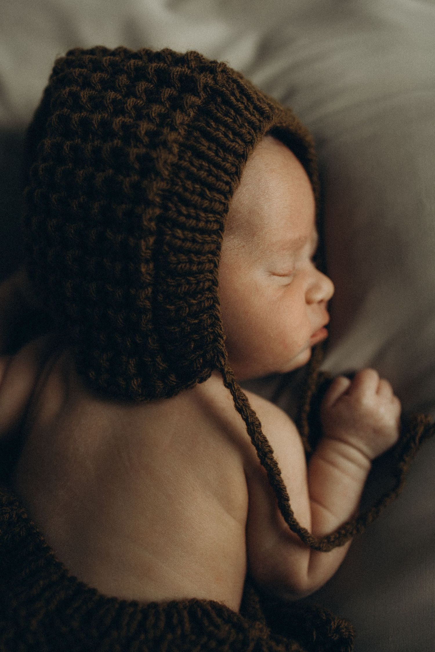 Newborn baby sleeping in a dark brown knit bonnet and outfit, close-up portrait photography.