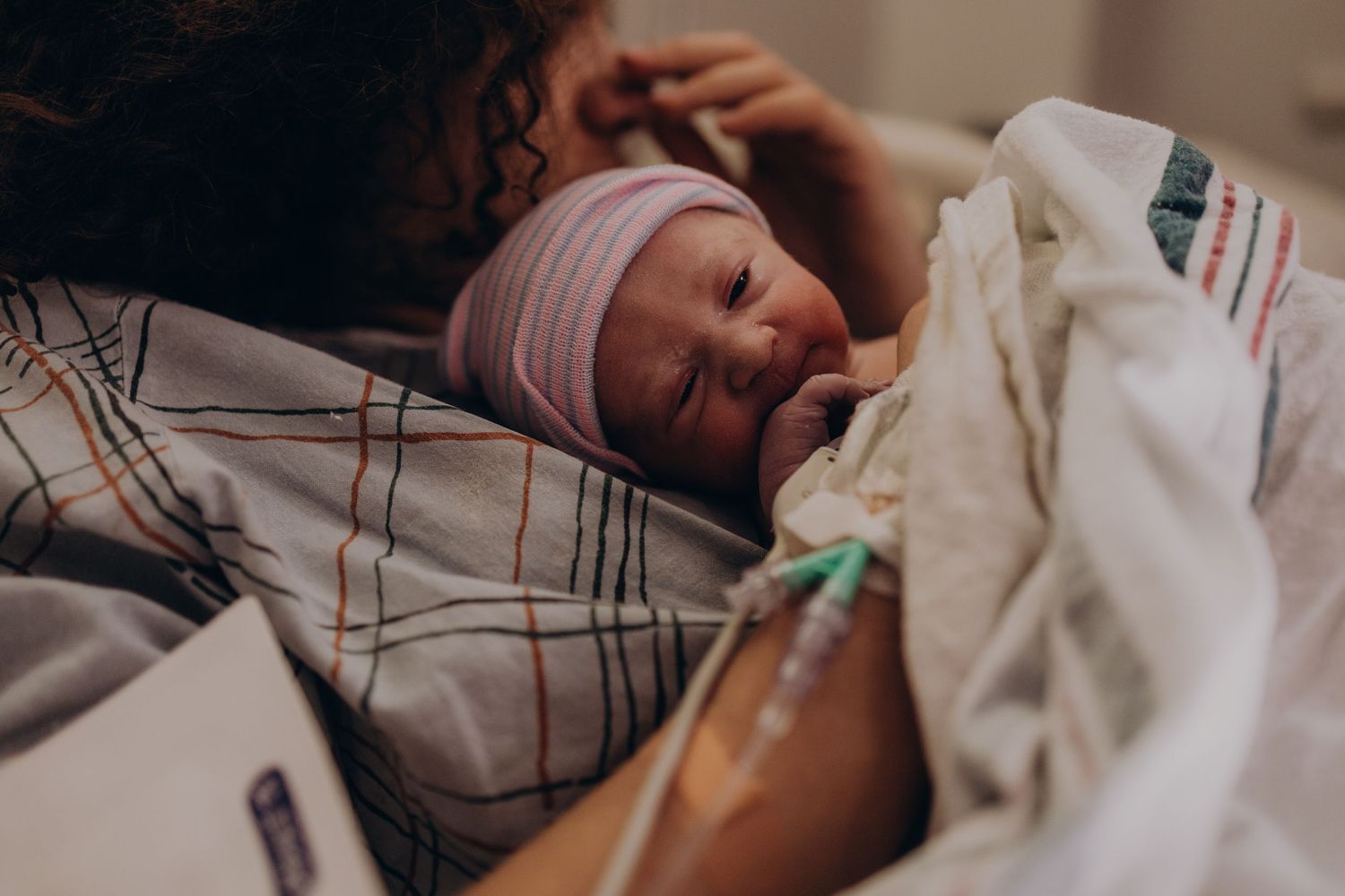 Mother holding her newborn baby in a hospital bed, baby wearing a pink striped hat after birth.