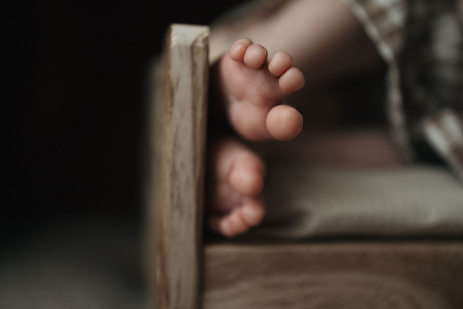 Close-up of tiny newborn baby feet dangling over the edge of a rustic wooden prop bed.