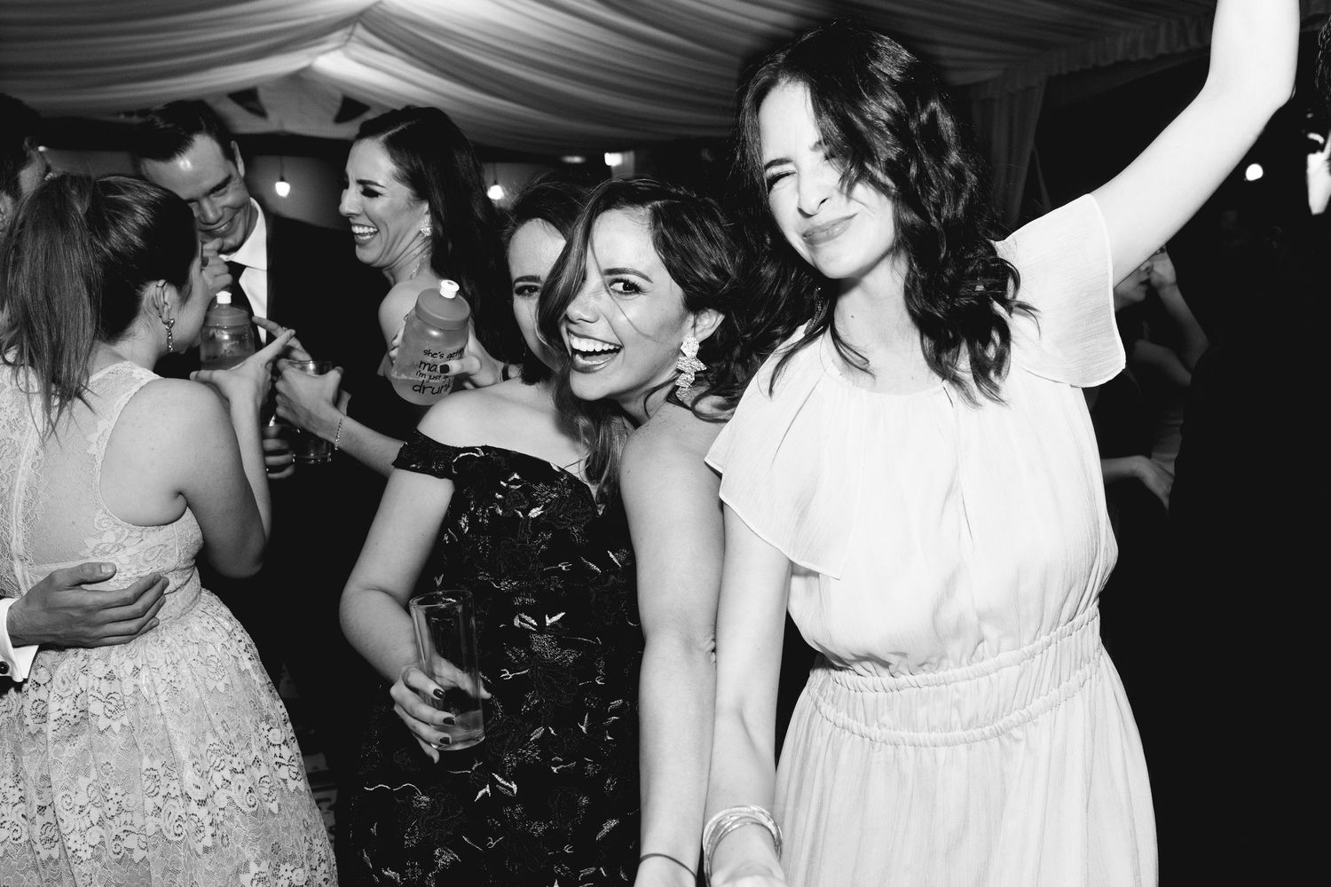 Party guests dancing and celebrating under white draped tent ceiling at night.