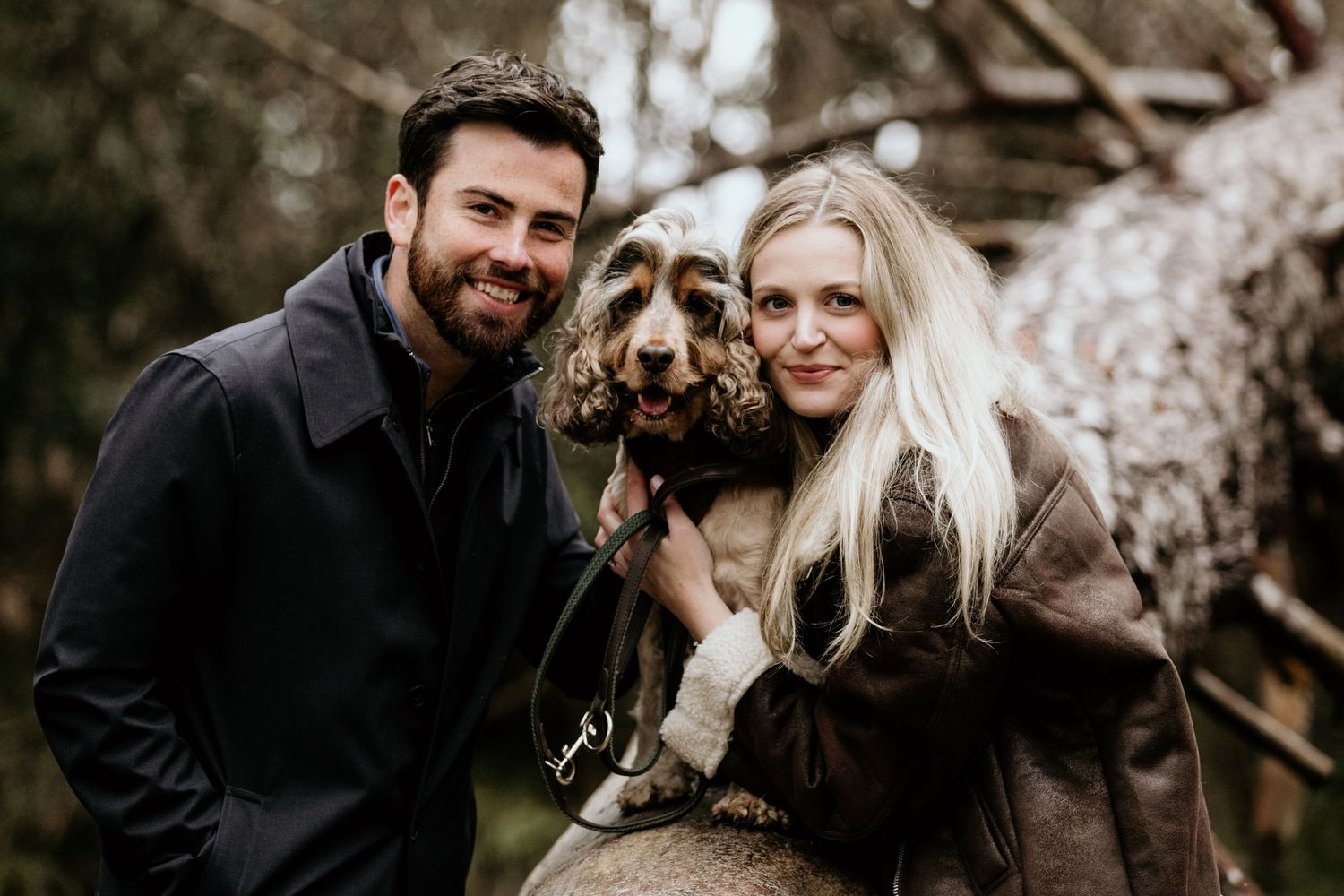 couple with there dog sitting on a tree trunk