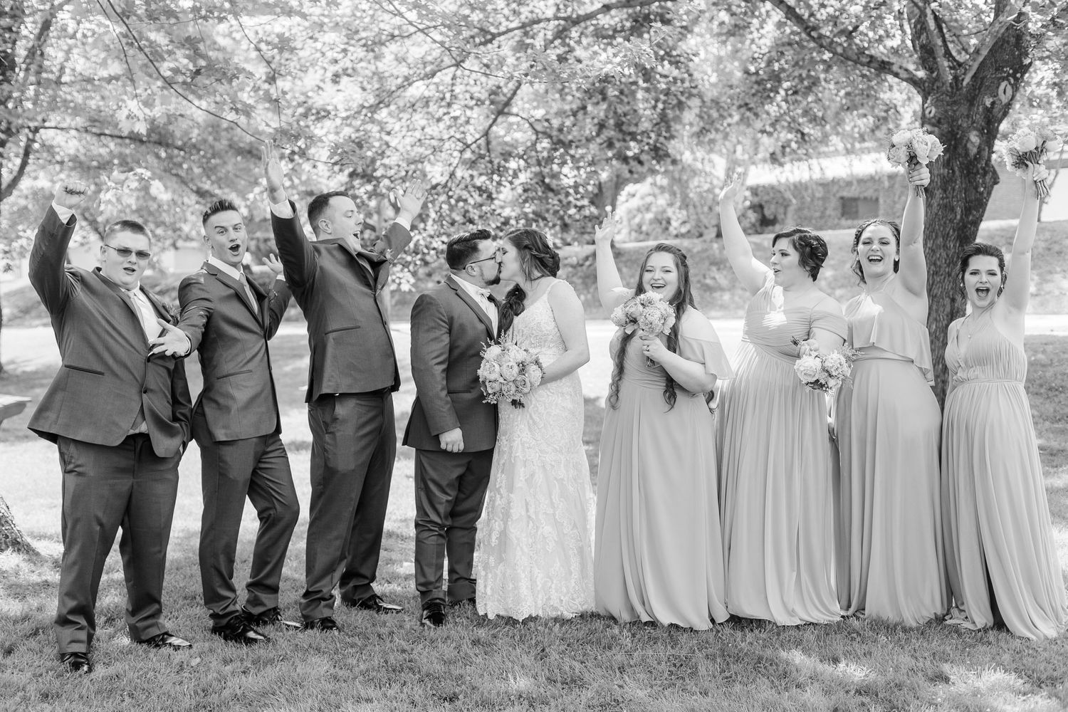 Black and white photo of wedding party lined up outdoors under trees.