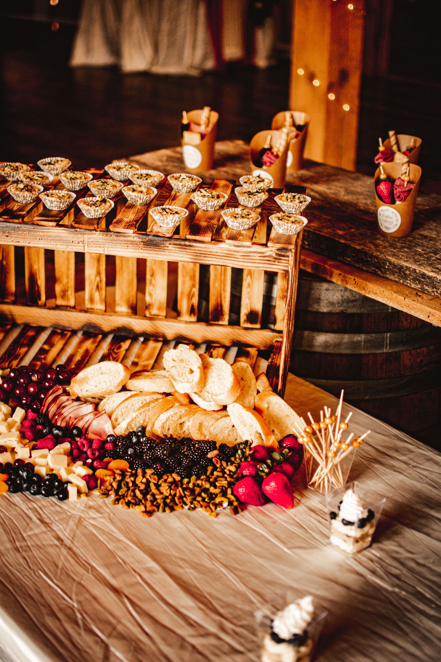 Rustic wedding dessert display featuring artisan pastries and fresh berries on wooden crates and barrels.