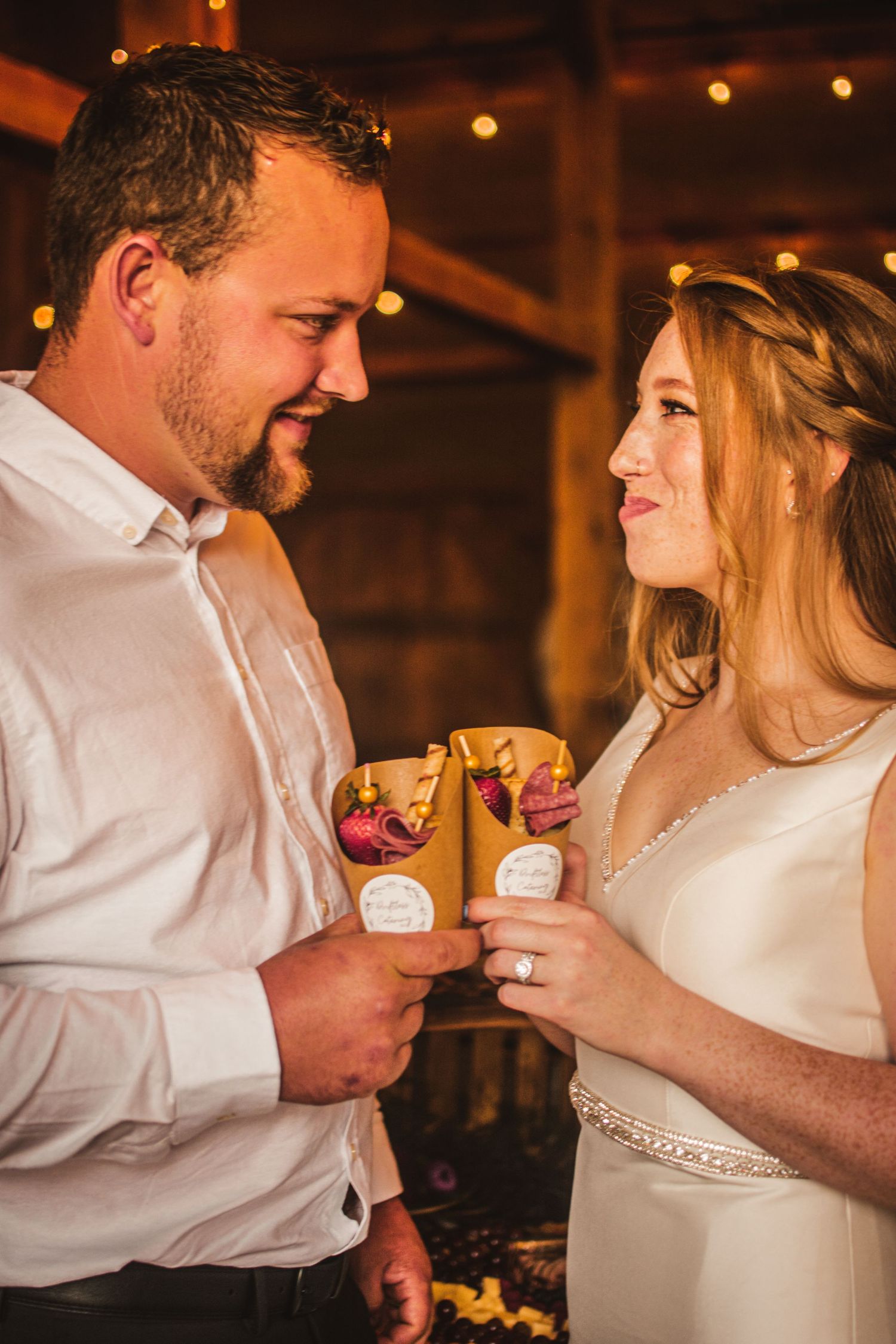 Couple sharing drinks in rustic reception venue with string lights.
