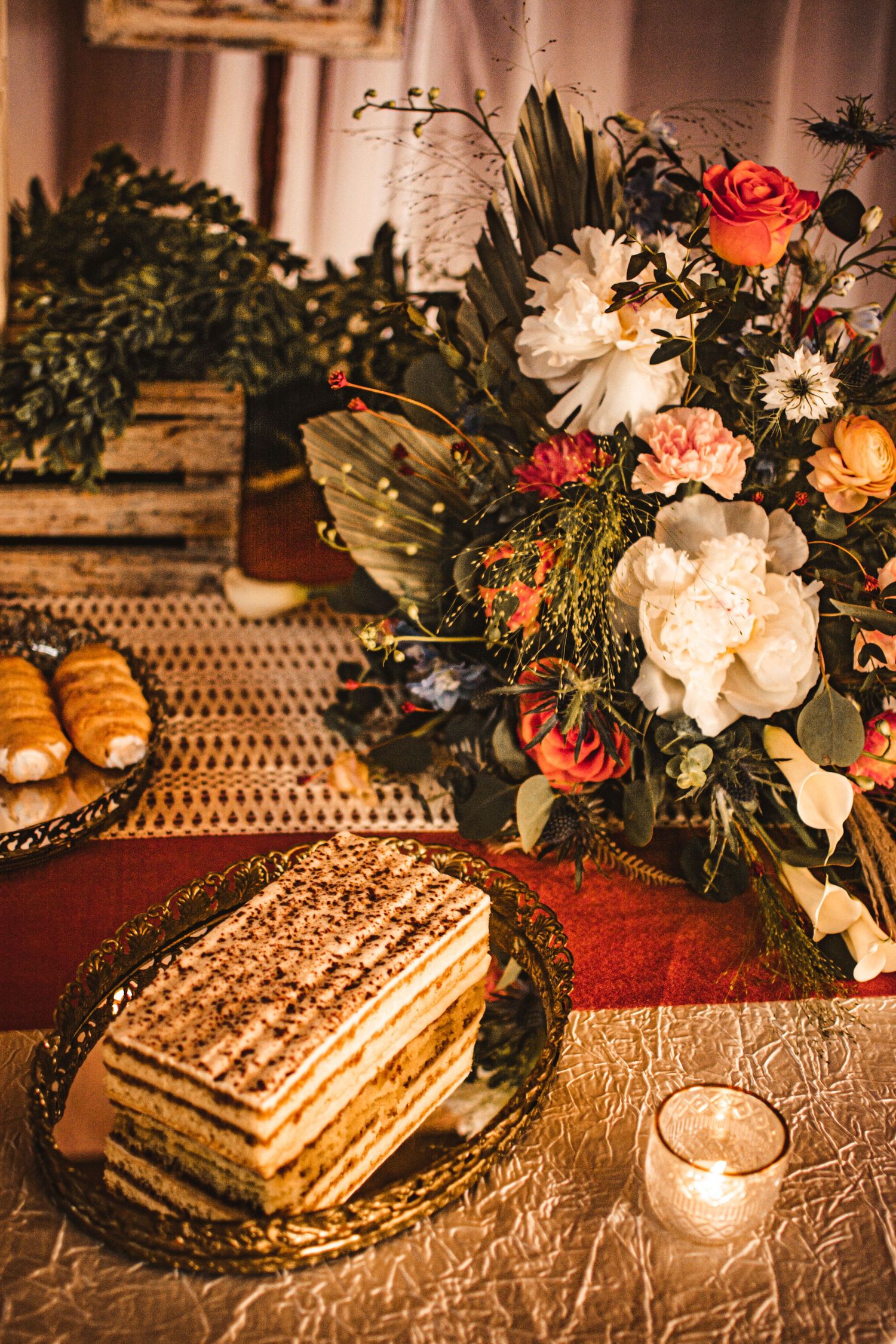 Elegant floral centerpiece with coral roses next to layered cake and pastries on lace tablecloth.