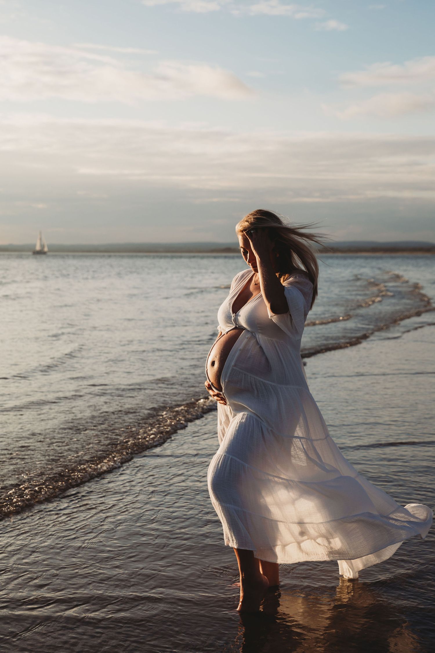 Figure in flowing white dress twirling by the ocean shore at sunset.