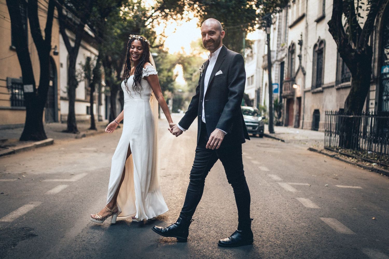 Couple in wedding attire walking playfully down a city street.