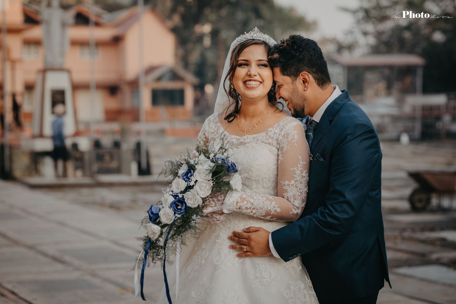 Romantic wedding couple posing outdoors at sunset with blue floral bouquet.