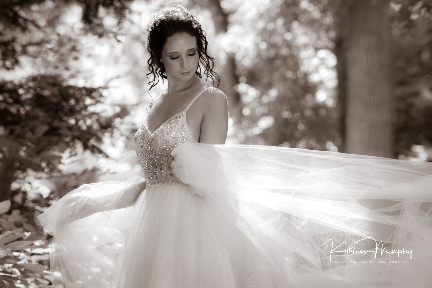 Elegant bridal portrait in black and white showing flowing tulle dress in a forest setting.