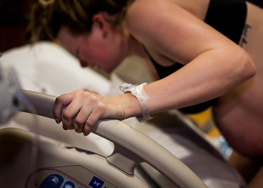 A patient grips the hospital bed rail during labor with a medical bracelet visible on their wrist.