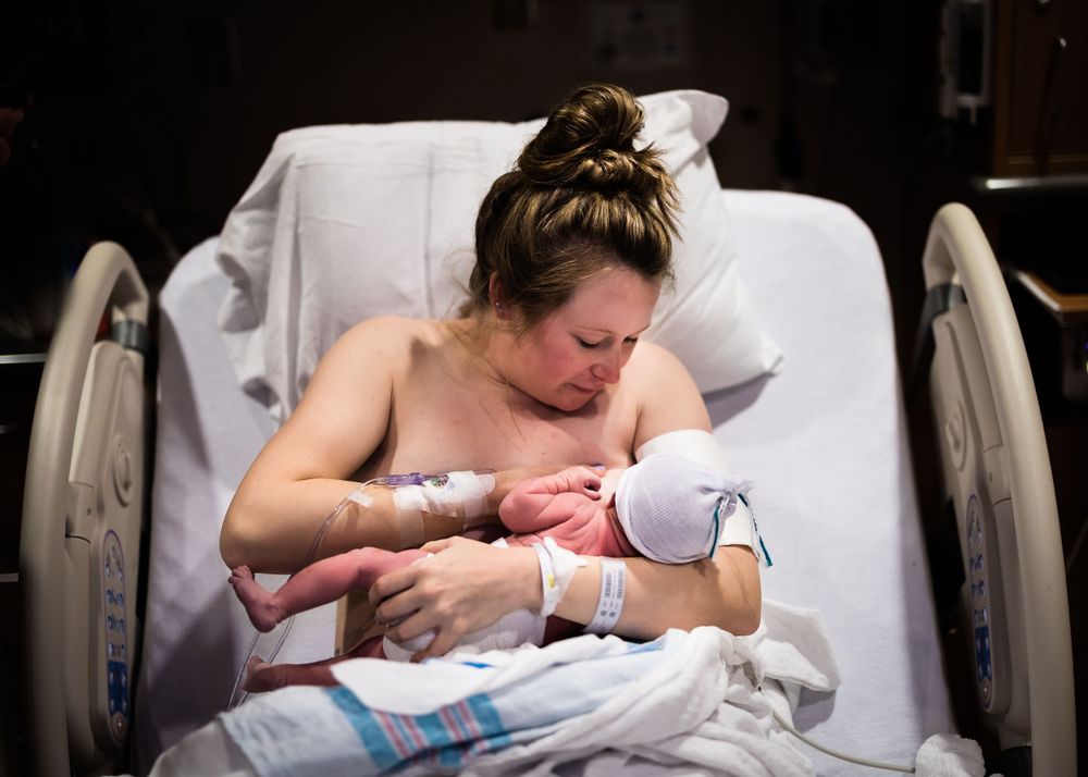 A new parent cradles their newborn in a hospital bed while wearing a medical bracelet.