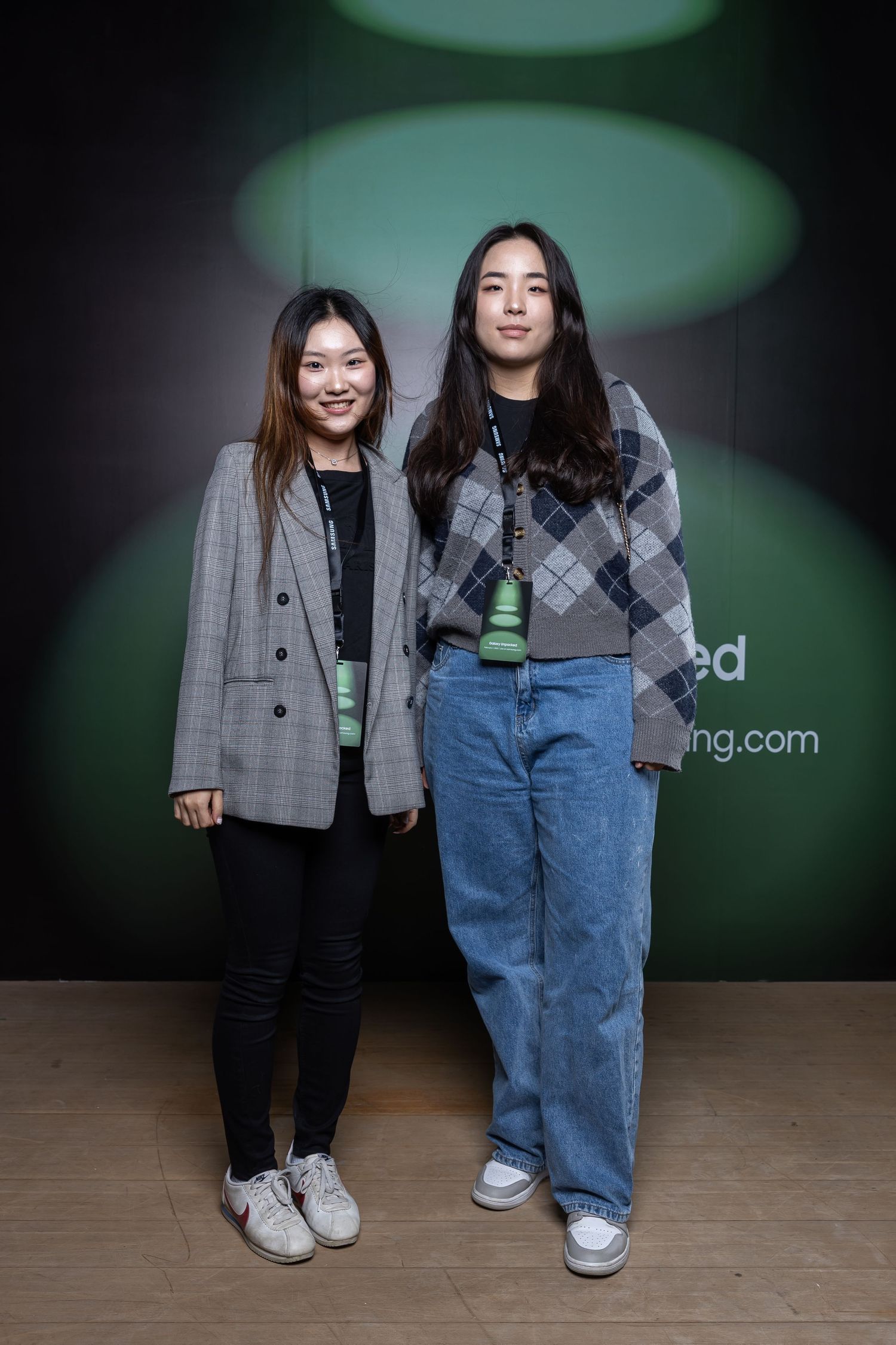 Two people posing against a dark background with green spotlight circles.