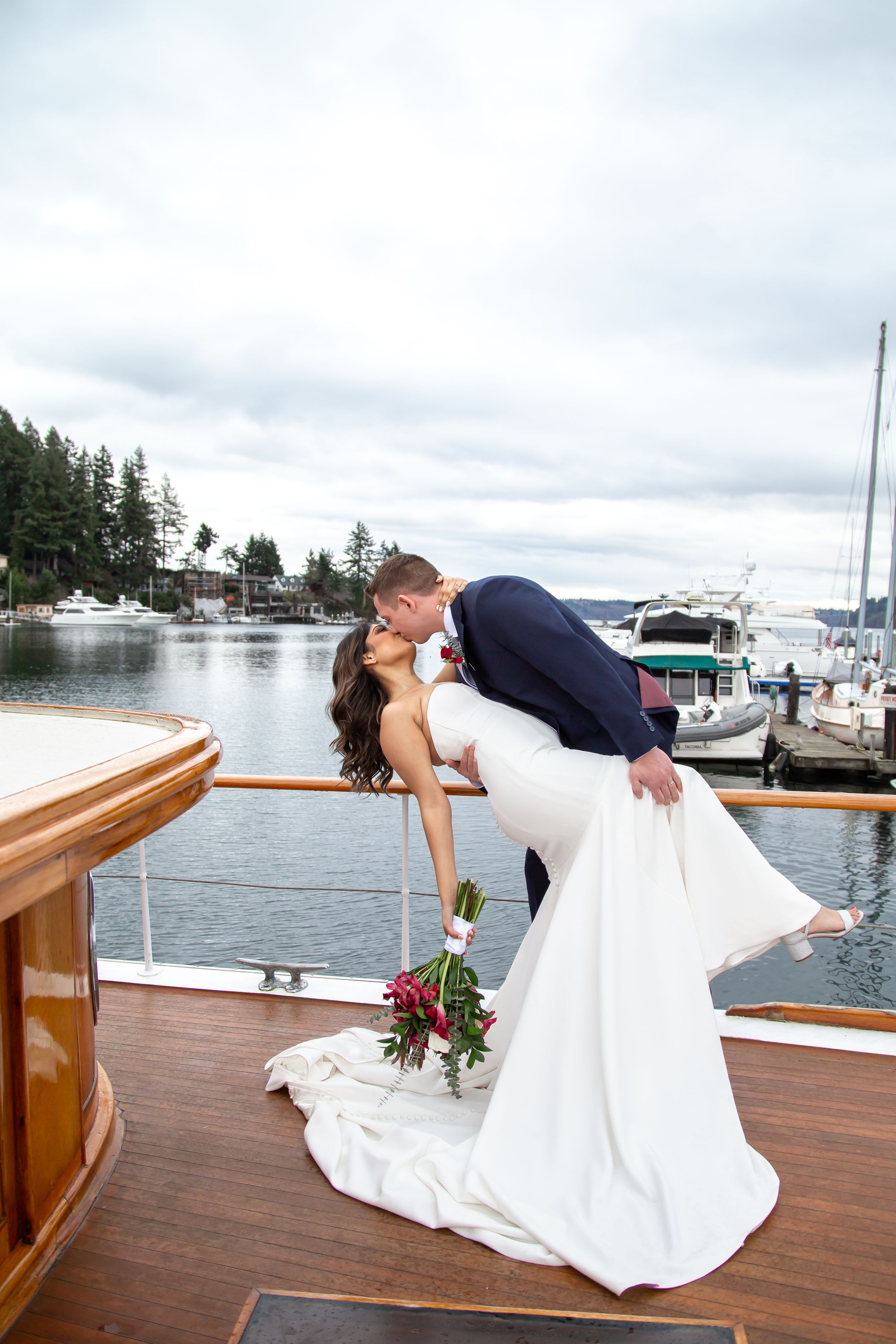 Romantic wedding couple sharing intimate moment on boat deck overlooking marina at sunset.