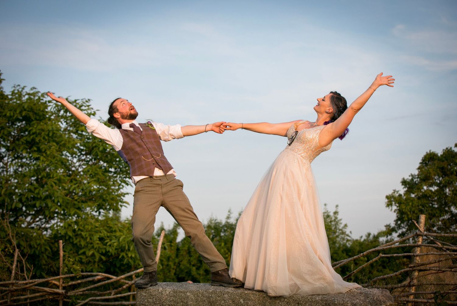 Playful wedding couple striking fun poses in an outdoor setting at sunset.