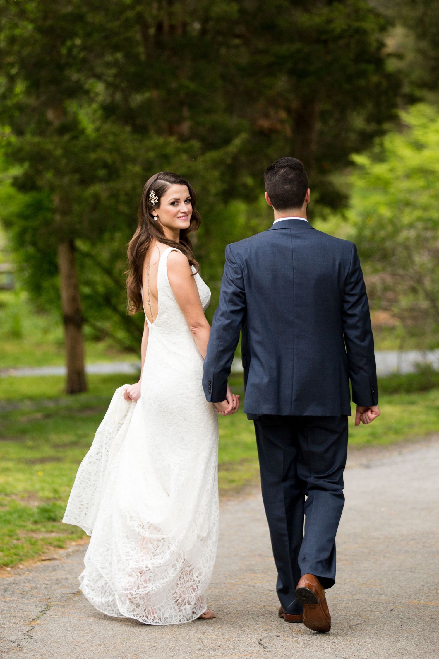 A couple walking along a scenic park path in wedding attire.