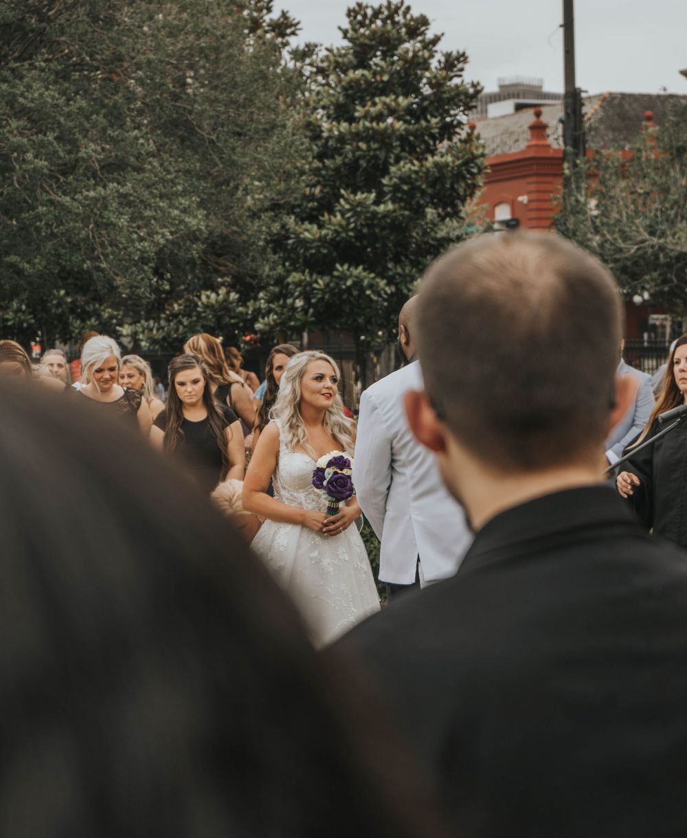 Wedding guests gather outdoors watching a ceremony with a distinctive brick building in the background.