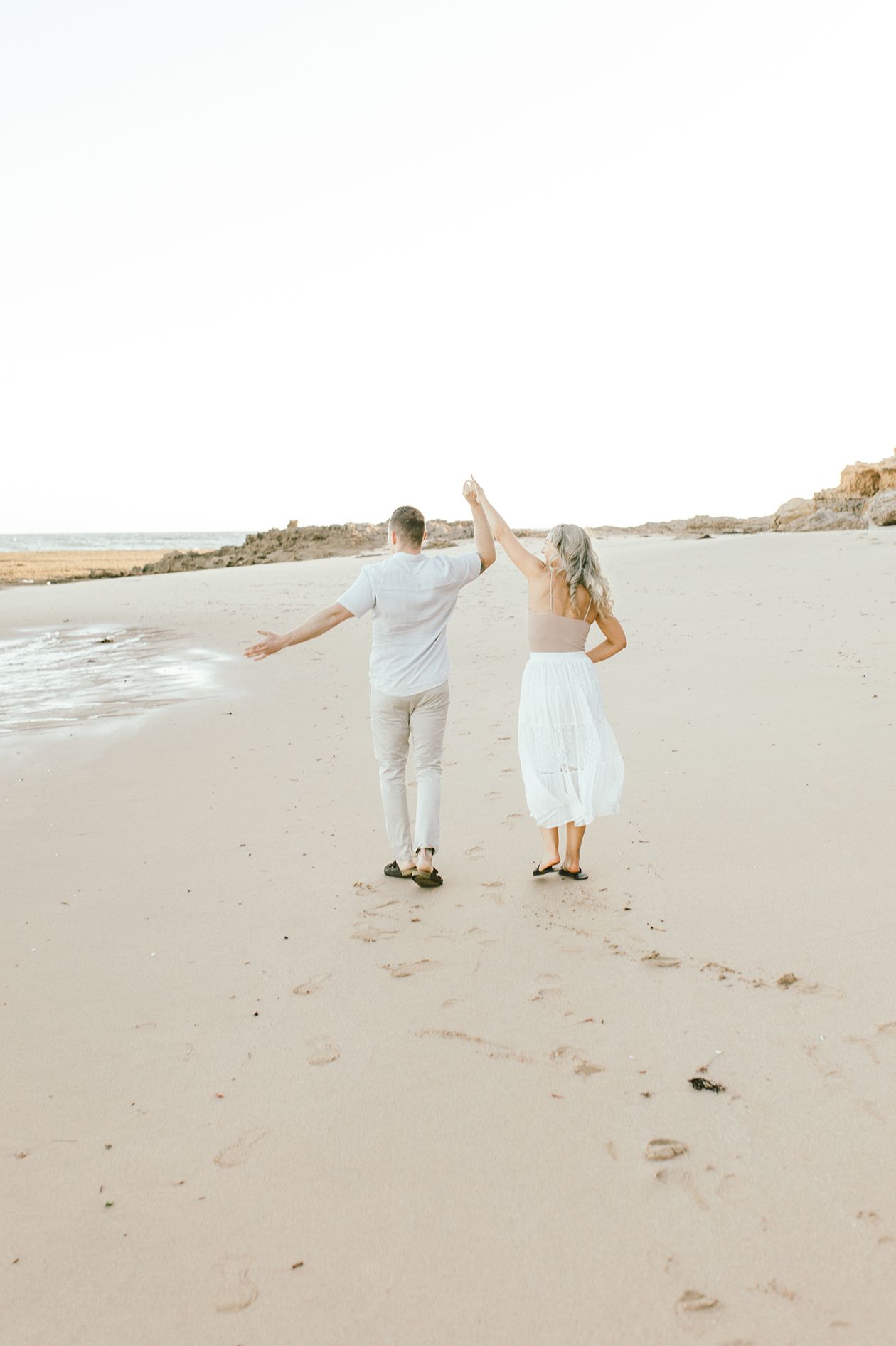 Two people with arms raised dancing joyfully on a beach at sunset.