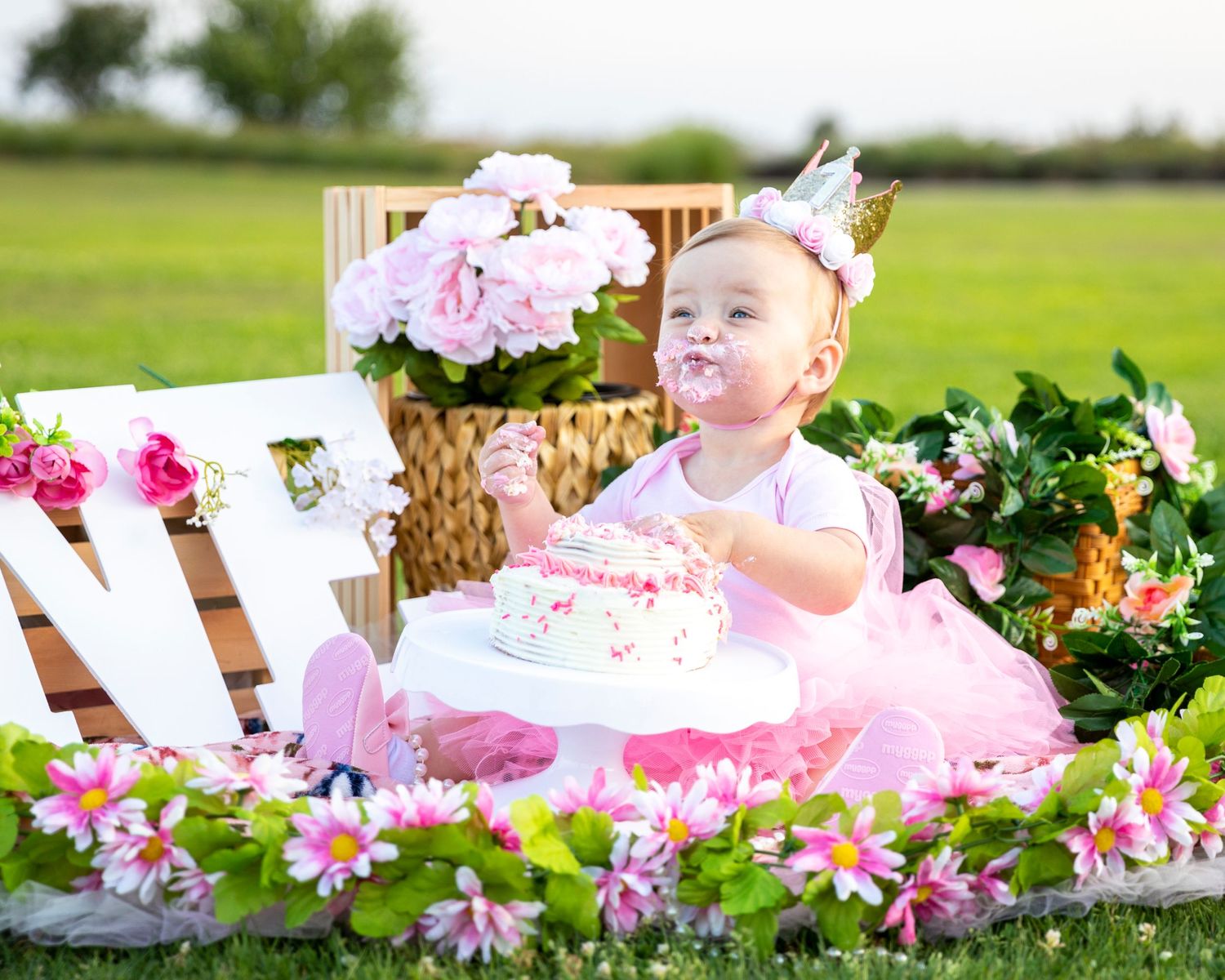 birthday photoshoot with Baby girl in pink tutu celebrating first birthday with cake surrounded by flowers outdoors.