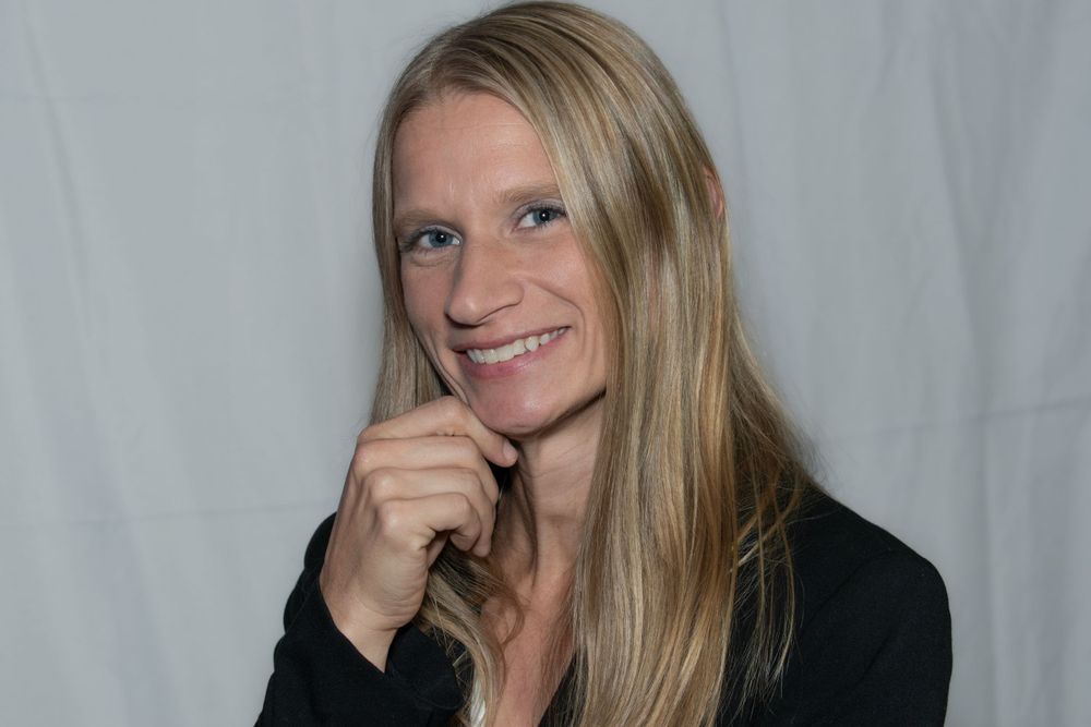 A person in a black jacket poses thoughtfully against a light background.