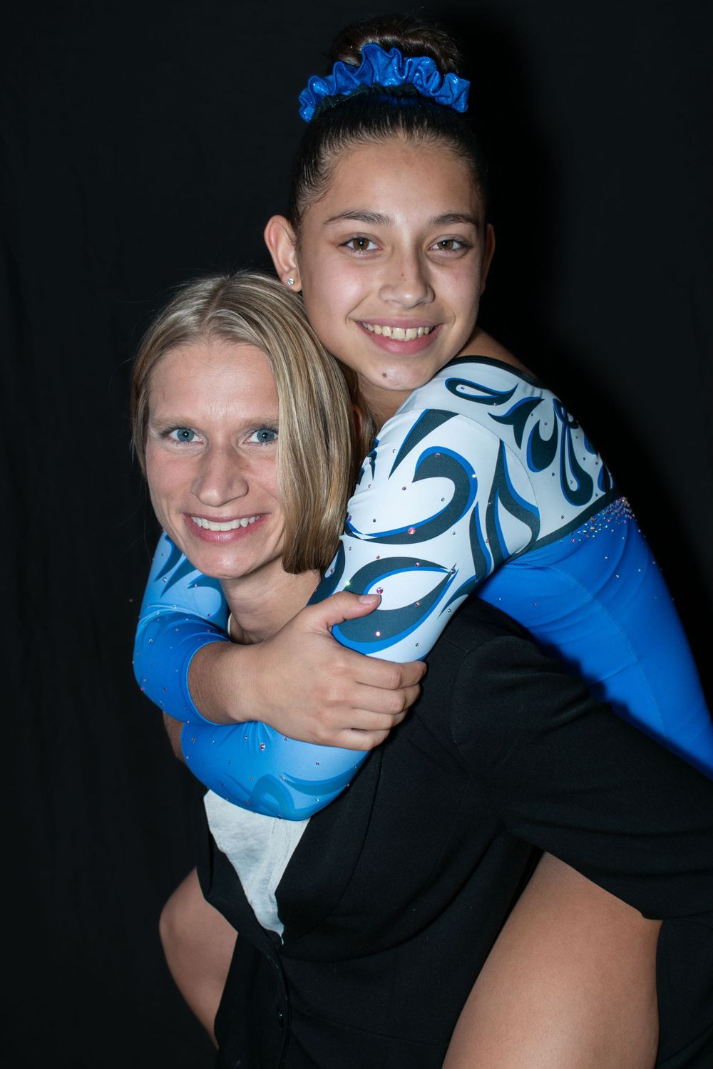 Two people in athletic wear share a playful piggyback pose against a dark background.