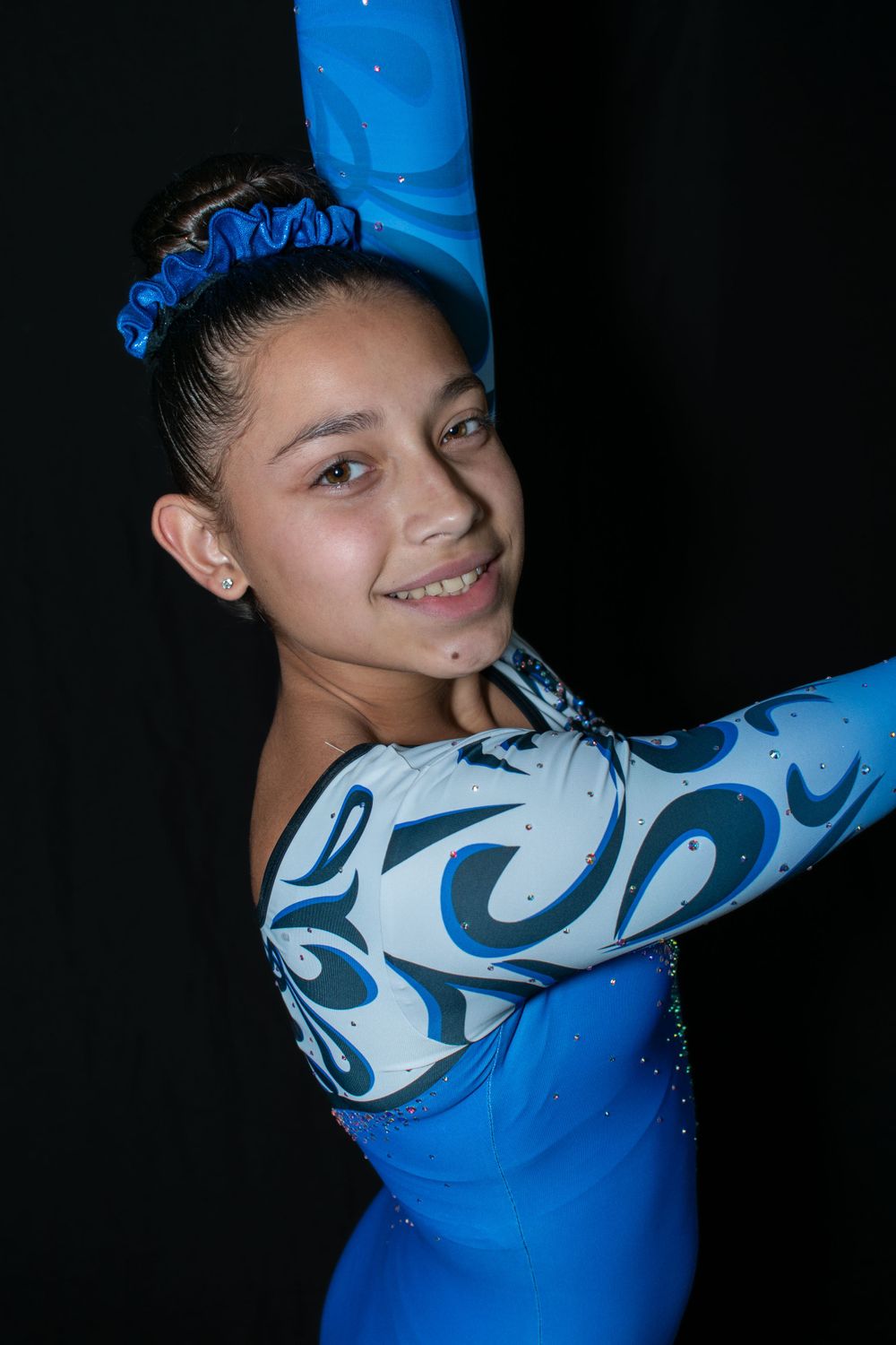 Gymnast in sparkling blue leotard with swirl pattern smiling during performance.