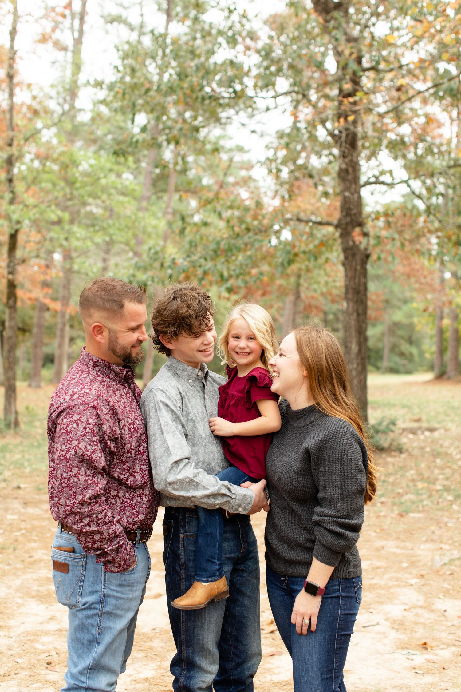 A casual family photo shoot in a wooded area with fall colors in the background.