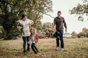 Bishops Stortford family photographer, mother and father walking and swing their two girls whilst mother holds baby