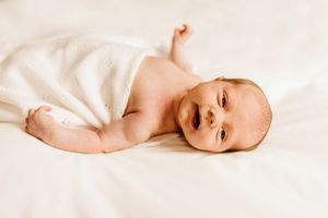Bishops Stortford baby photographer, Hertfordshire, newborn baby lying on bed in blanket laughing