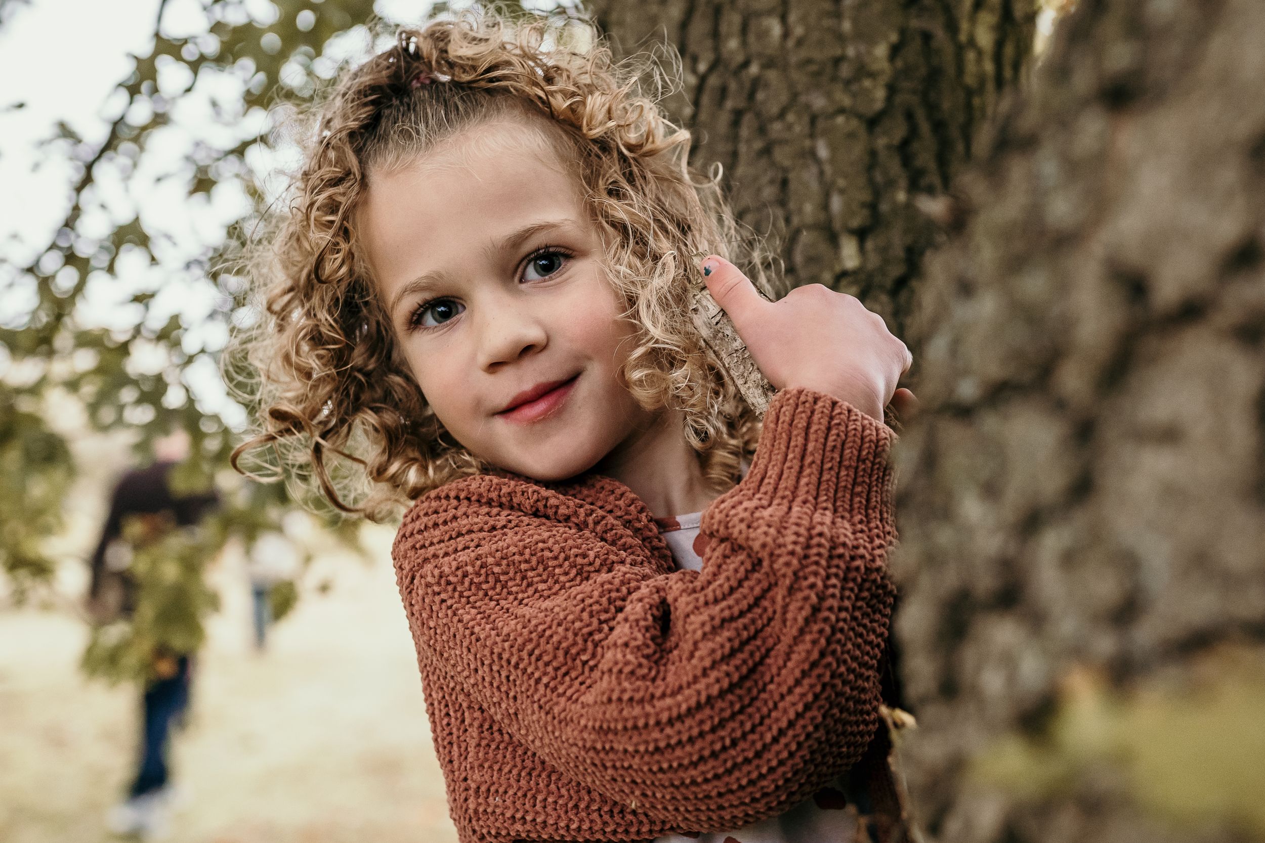 Bishops Stortford family photographer, Hertfordshire, close up of young girl peaking out from behind a tree, natural