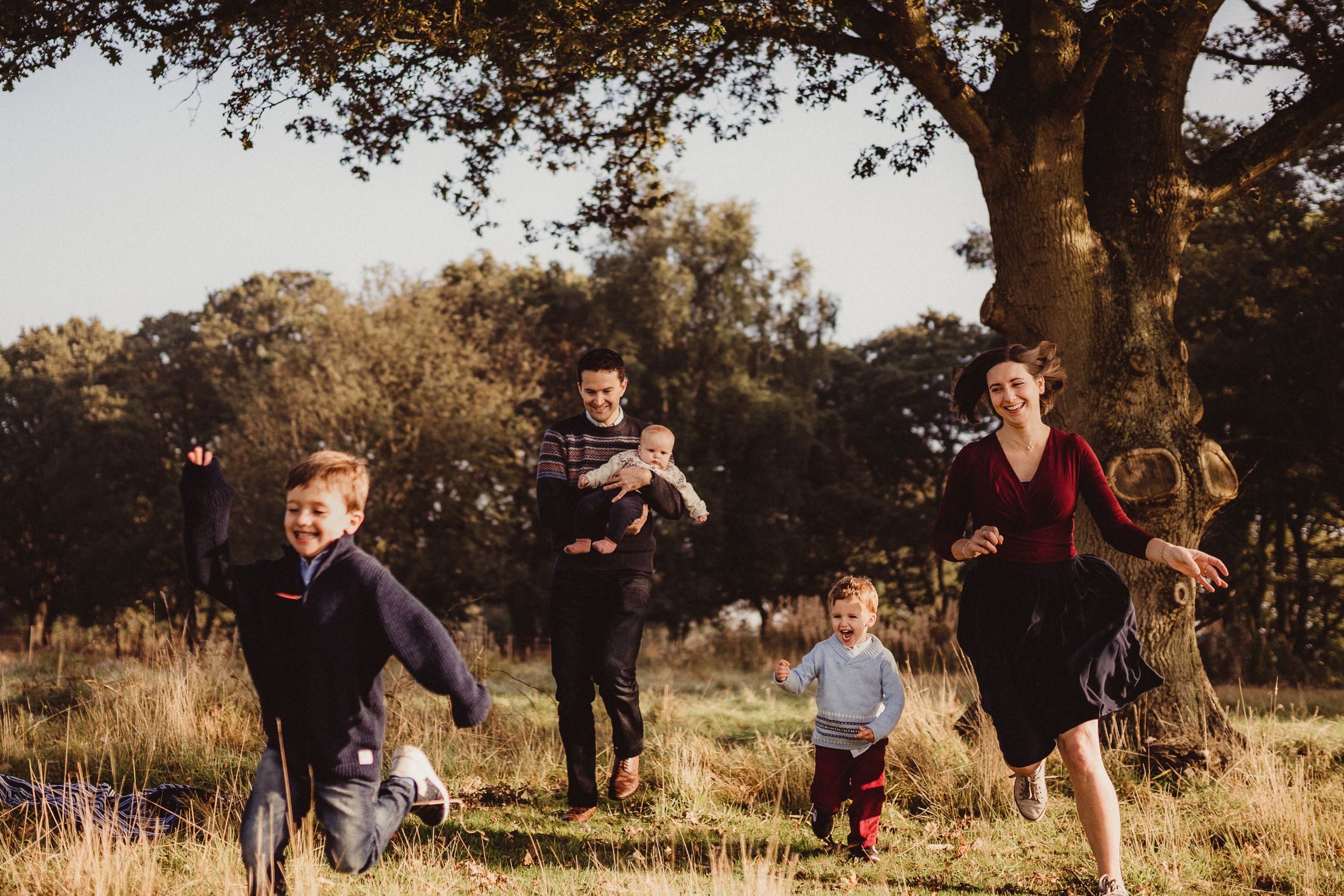 Bishops Stortford family photographer, Hertfordshire, parents chasing their two young boys outside, fun family shoot