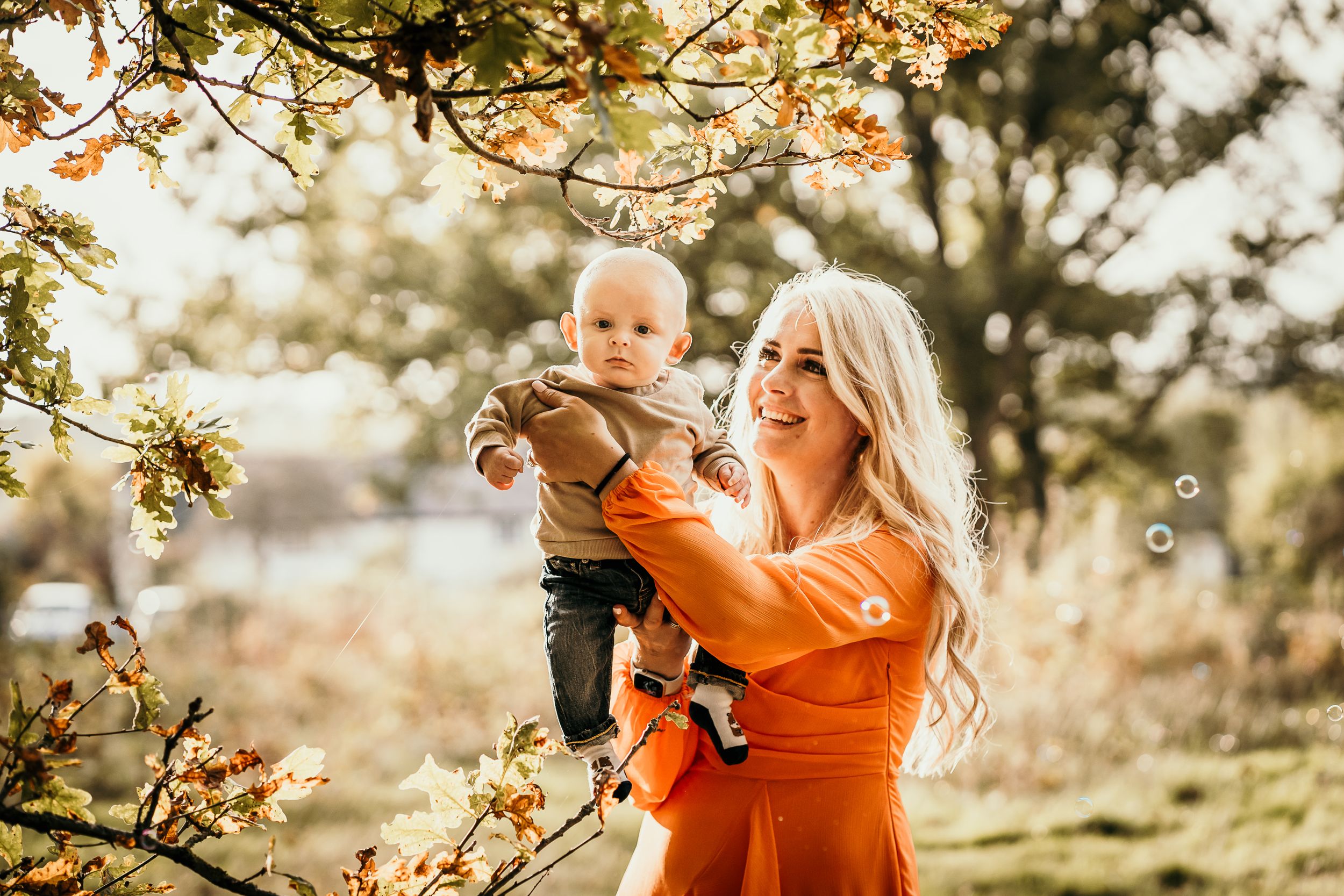Bishops Stortford family photographer, Hertfordshire, mother holding up her baby amongst the golden autumn leaves