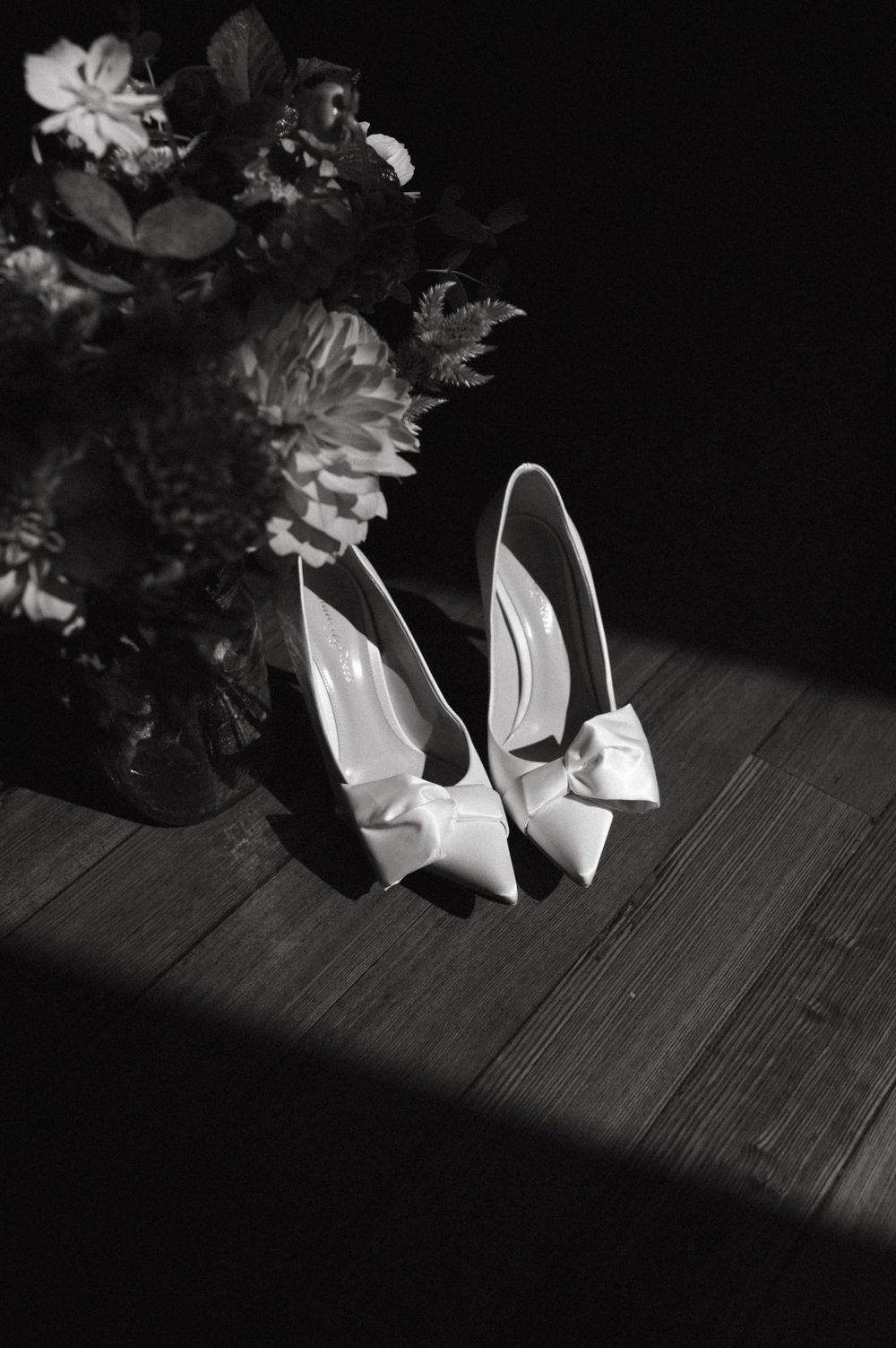 Elegant white bridal shoes with bows photographed in dramatic black and white lighting.