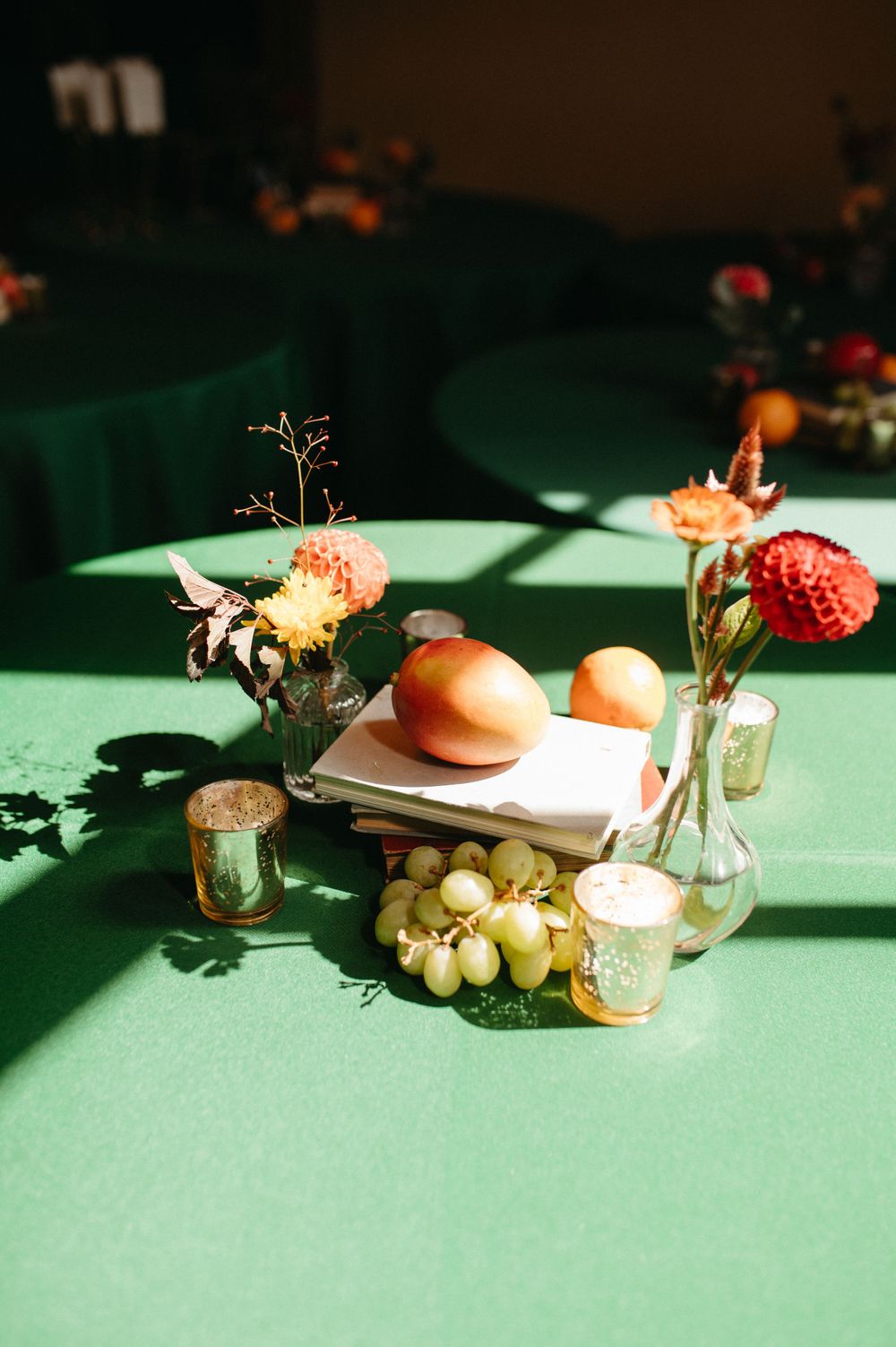 Wedding reception table with fruit, flowers and candles on green tablecloth in dramatic lighting.
