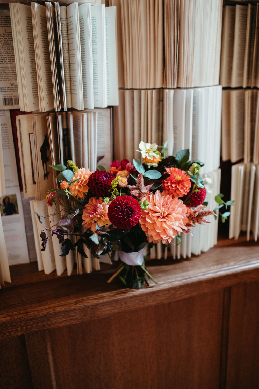 Vibrant fall-colored wedding bouquet with dahlias and roses sitting in front of vintage books.