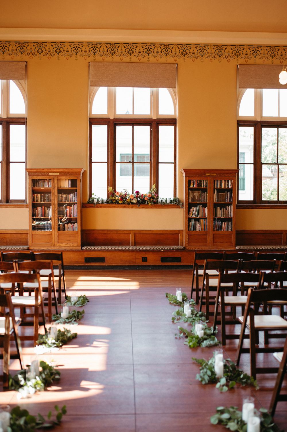 Library wedding ceremony setup with wooden chairs and floral aisle decorations.