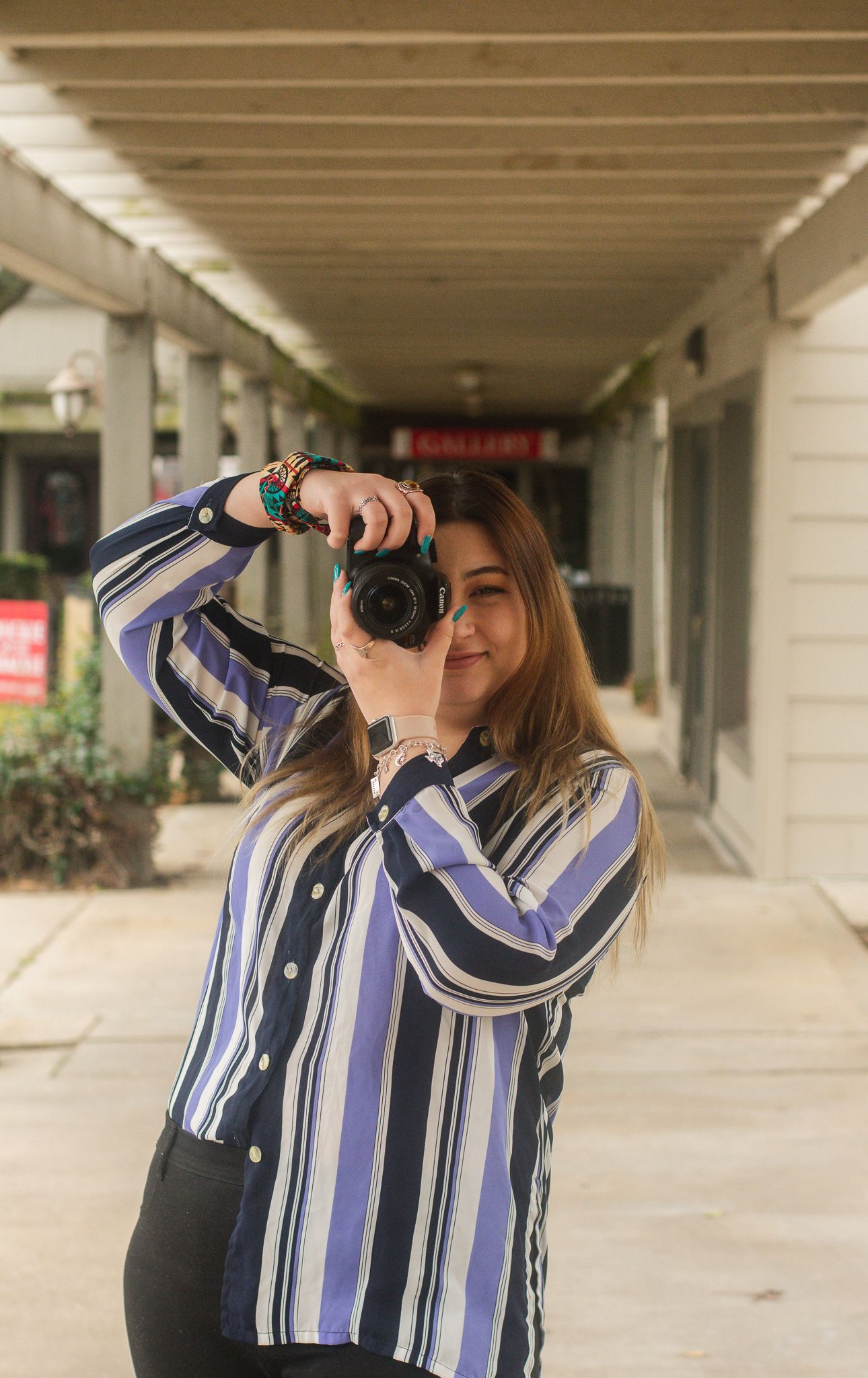 Photographer in striped button-down shirt taking pictures in covered walkway.