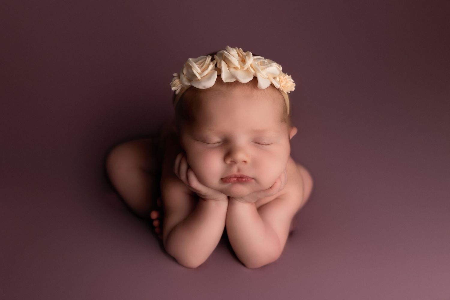 Artistic newborn photography with baby posed on burgundy backdrop with floral accessories.