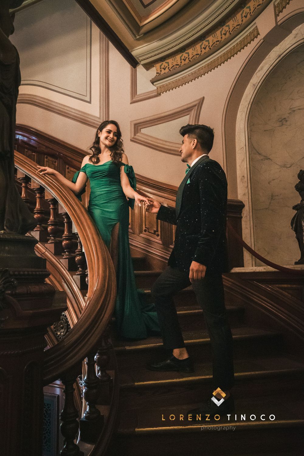 A couple in elegant attire poses on a grand curved staircase in a historic building.