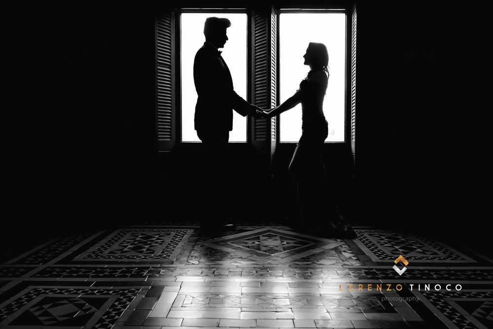 A silhouetted couple holds hands in front of a backlit window creating a dramatic scene.
