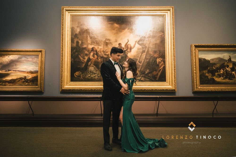 A romantic photoshoot in an art gallery features a couple in formal wear standing in front of classical paintings.