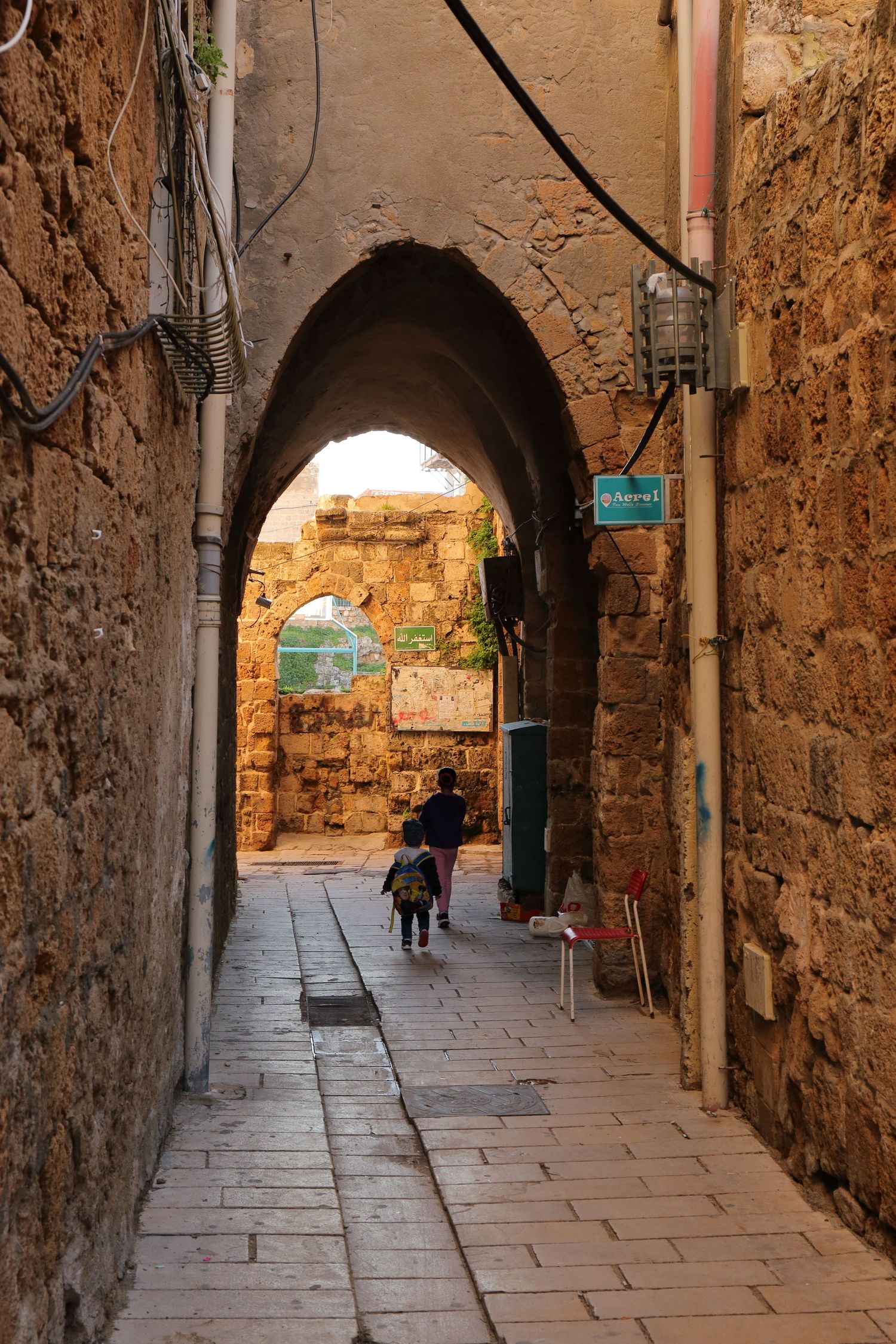 Ancient stone archway in narrow alley of old city with person walking through.