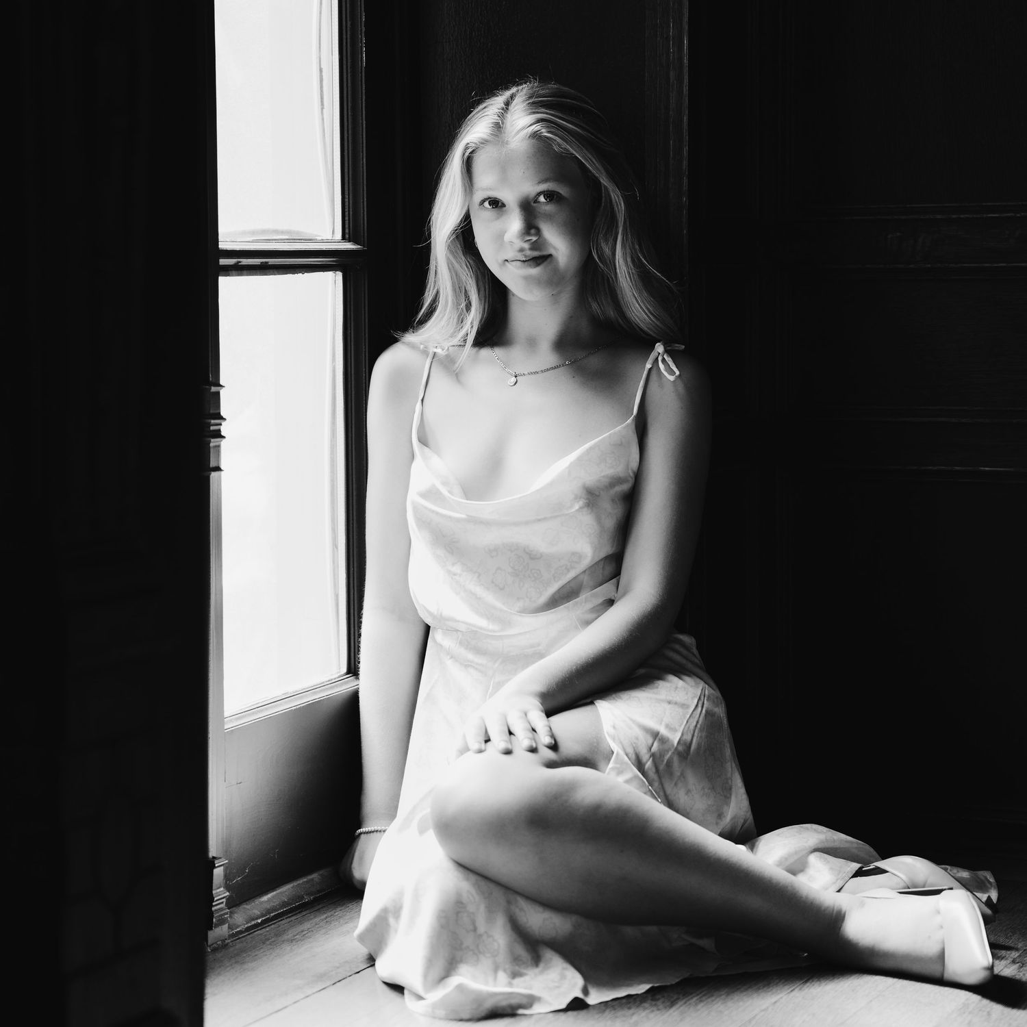 black and white senior portrait of young girl in dress leaning against bright window, shot by Milwaukee senior photographer Rachel Dickman.
