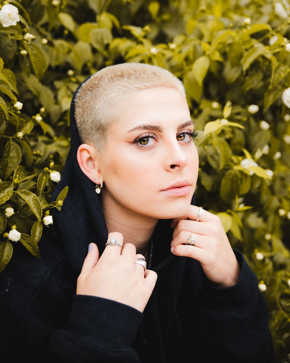 Close-up portrait with short blonde hair against green leafy background.