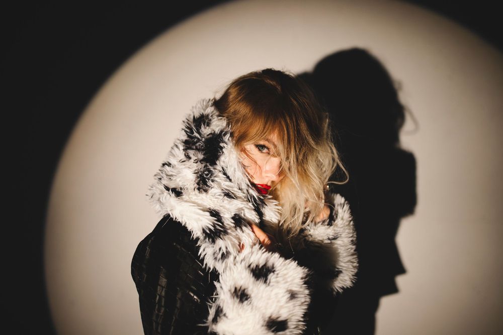 Artistic portrait with black fur collar and dramatic shadow against light background.