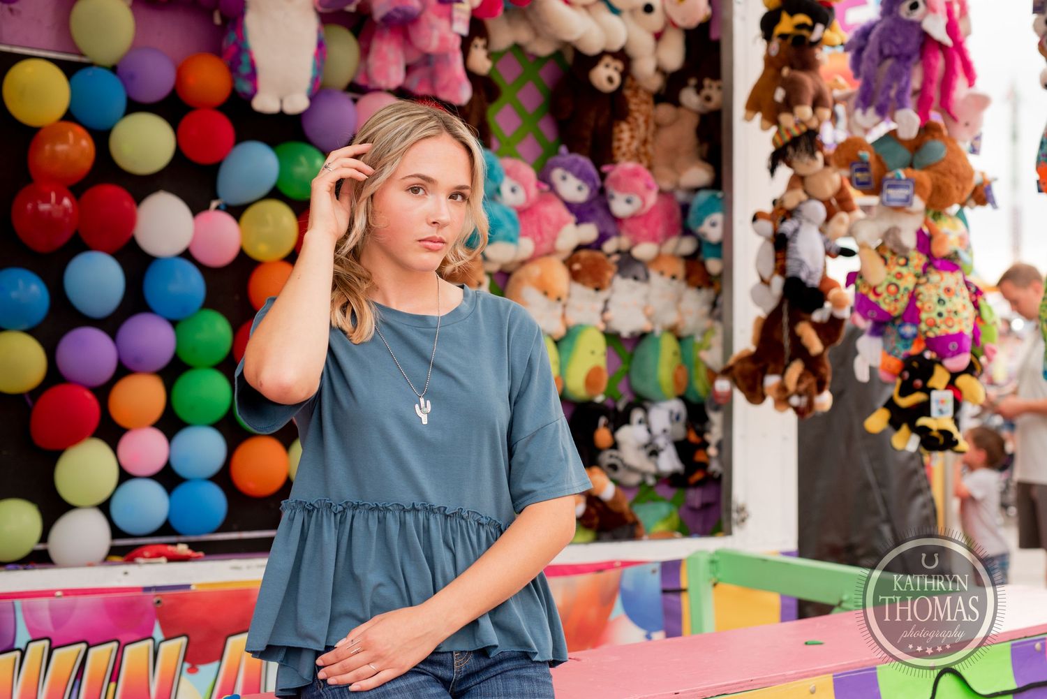 Person posing against vibrant carnival backdrop with balloons and plush toys.