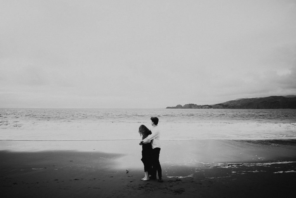 Two silhouettes embrace on a moody beach with dramatic lighting and waves.